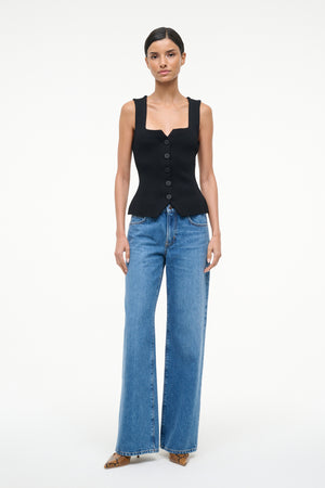 Woman wearing a black sleeveless top and blue jeans on a white background