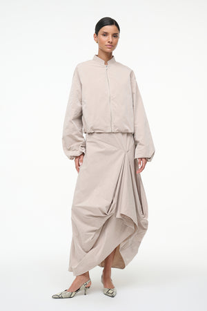 Woman wearing a beige outfit with a long skirt on a white background
