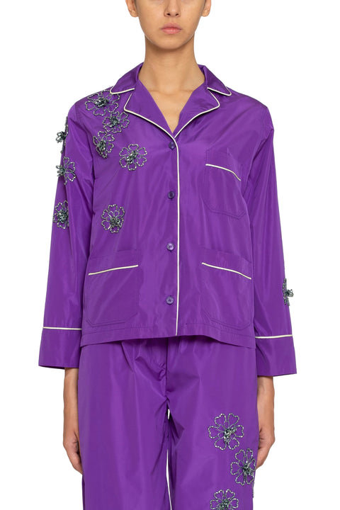 Detail shot of woman wearing a purple button down pajama shirt with floral embellishments and a matching maxi skirt.