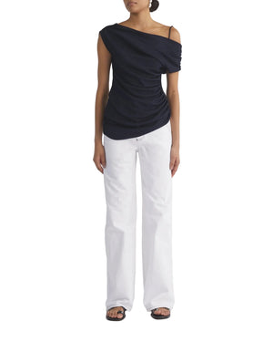 Person wearing a black one-shoulder top and white jeans on a white background