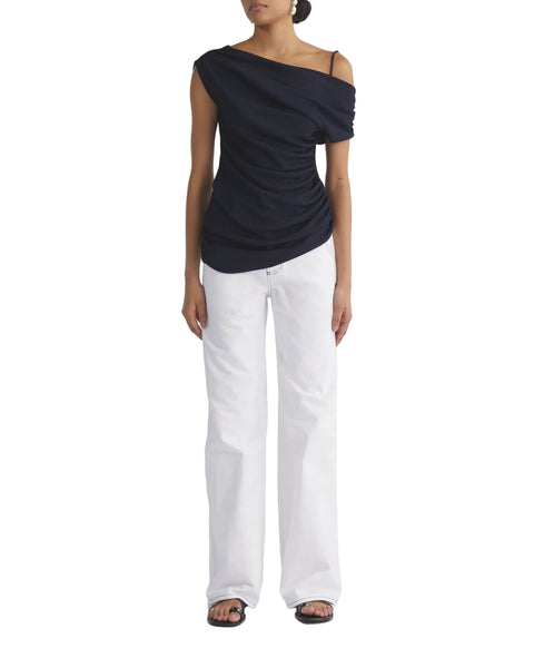 Person wearing a black one-shoulder top and white jeans on a white background