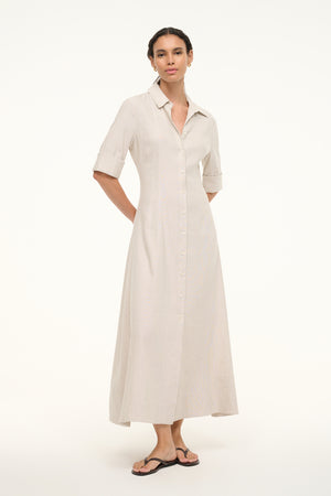 Woman wearing a cream linen maxi dress that features half sleeves, a collar, and button down detail down he front, paired with sandals.