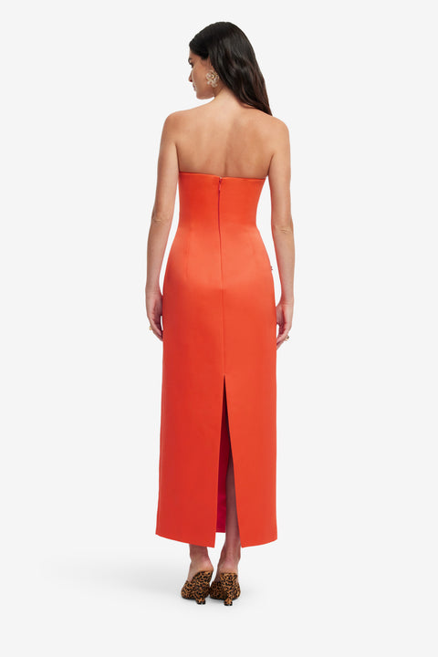 Woman showing back of an orange strapless dress with a slit on a white background