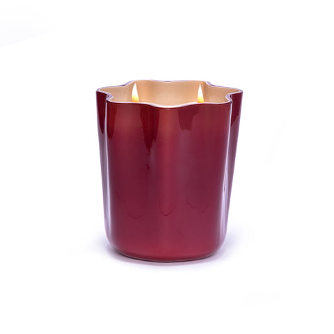 Red murano glass candle in scallop shape lit up.