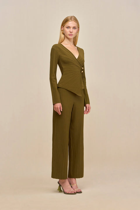 Side-facing woman wearing green ribbed wide-leg pants and a matching wrap top with gold hardware accents.