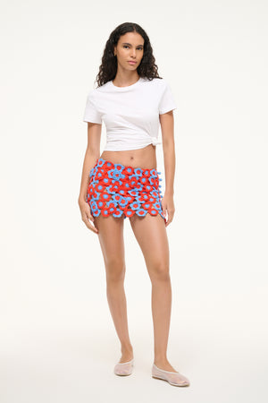 Woman wearing a red and blue floral crochet mini skirt with a white tee and flats.