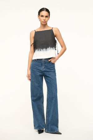 Woman wearing a black and white dip dye patterned boxy tank top that is open on the sides, paired with jeans.