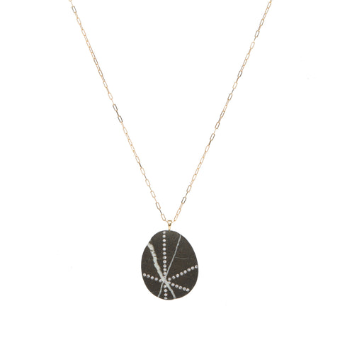 A black stone stone that features white streaks, accented by streaks of small round diamonds, suspended on a yellow gold paperclip chain.