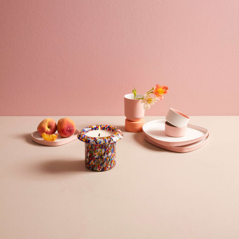 Lit multi colored glass candle set around pastel pink plates and cups.