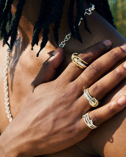 A man wearing a Spinelli Kilcollin Gemini ring that features a 1.7mm yellow gold band, a 3.8mm sterling silver textured band with two yellow gold annulets and one yellow gold annulet pave with diamonds, and a 2.3mm yellow gold band, connected by two yellow gold connectors.