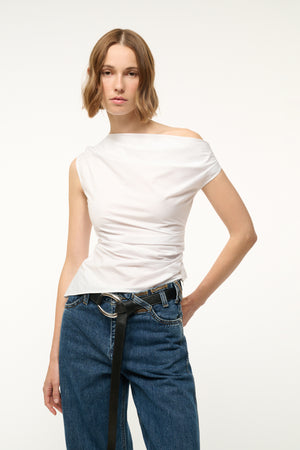 Woman wearing an asymmetrical white top with ruching throughout the bodice.