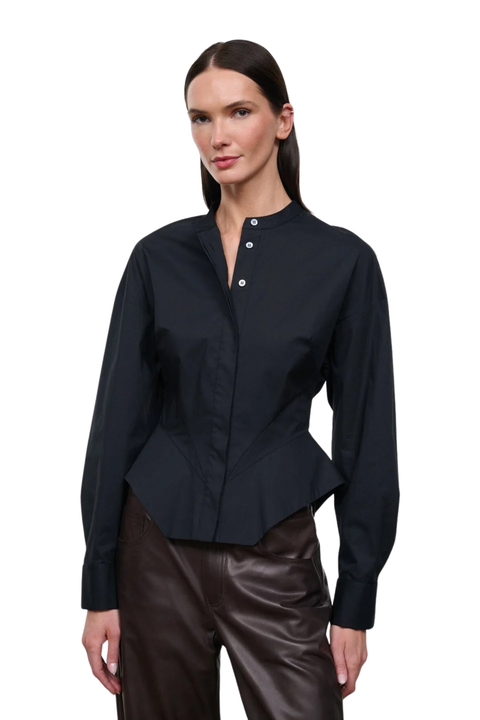 A woman modeling a black long-sleeve button-front blouse with a stand collar and peplum hem, paired with dark brown pants, against a plain white background.