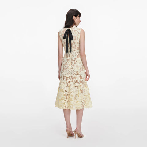 Woman facing away showing back of yellow lace dress with a black bow on a white background