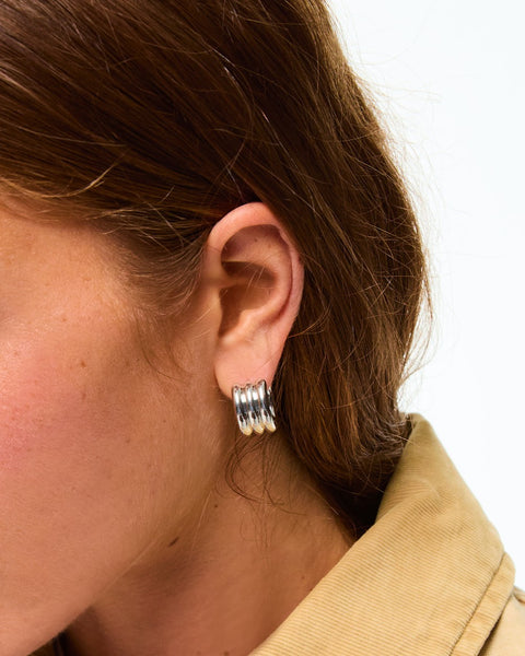 Woman wearing a silver-toned huggie earring that features a triple tube design.