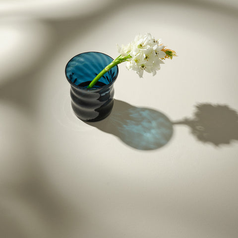 Blue glass vase with one floral stem inside.