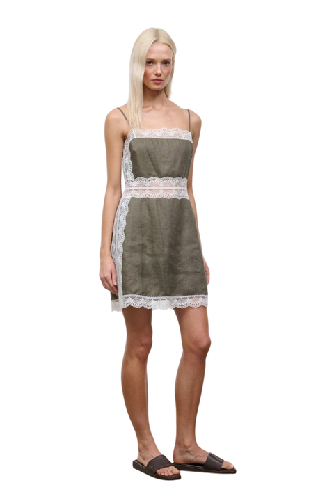 A woman wearing a taupe-green mini dress with white lace detailing on the waistline and neckline side