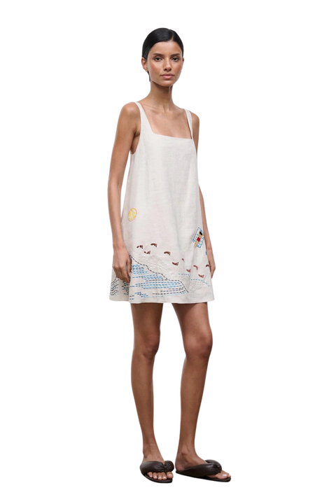A woman standing to the side angle wearing a mini dress with embroidered beach details