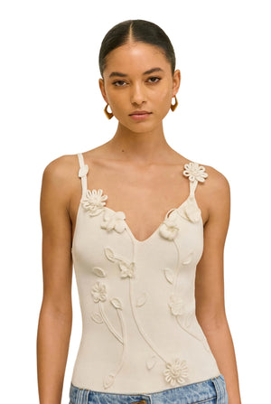 Woman wearing a cream-colored tank top with floral embellishments on a beige background