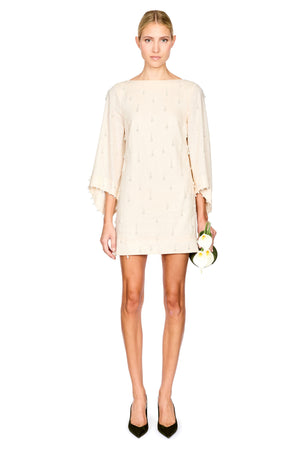 A woman modeling a short cream-colored mini dress with wide three-quarter sleeves and a subtle embroidered pearls, paired with black pointed-toe heels.