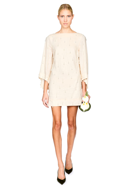 A woman modeling a short cream-colored mini dress with wide three-quarter sleeves and a subtle embroidered pearls, paired with black pointed-toe heels.