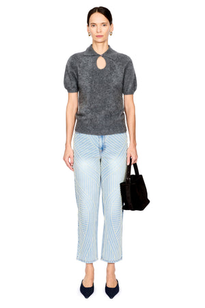 A model stands against a white background wearing a dark gray short-sleeve knit top with a keyhole cutout, light blue jeans with pearl detail, dark navy pointed shoes, and holding a dark brown handbag.