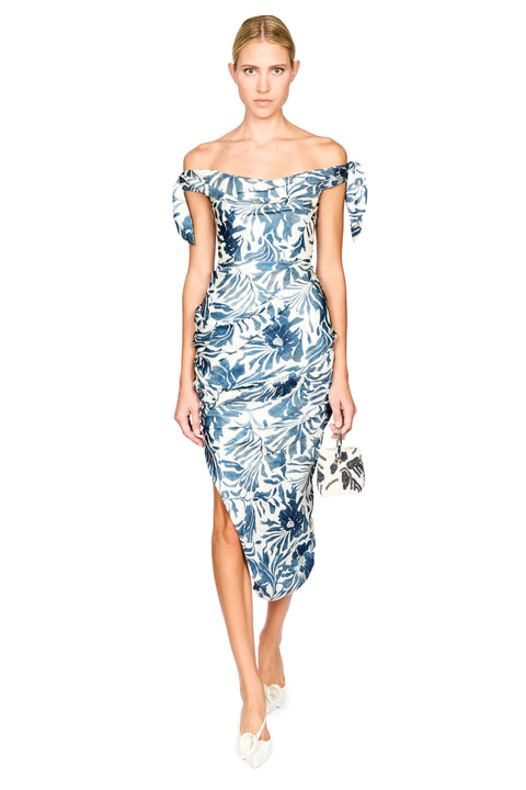 A model wearing an off-the-shoulder midi dress with a blue and white tropical floral print, holding a matching patterned clutch bag against a solid white background.