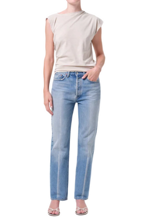 Person wearing light blue mid-rise, straight-leg jeans and a beige top on a white background with hand in pocket