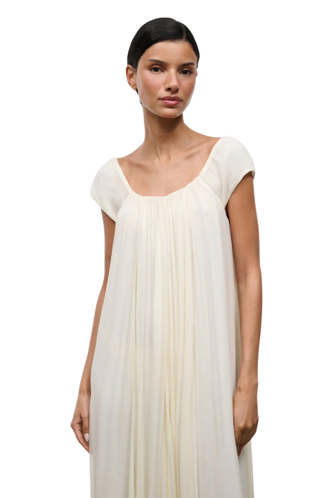 A close-up of a woman wearing a long ivory dress with short cap sleeves and an elastic neckline