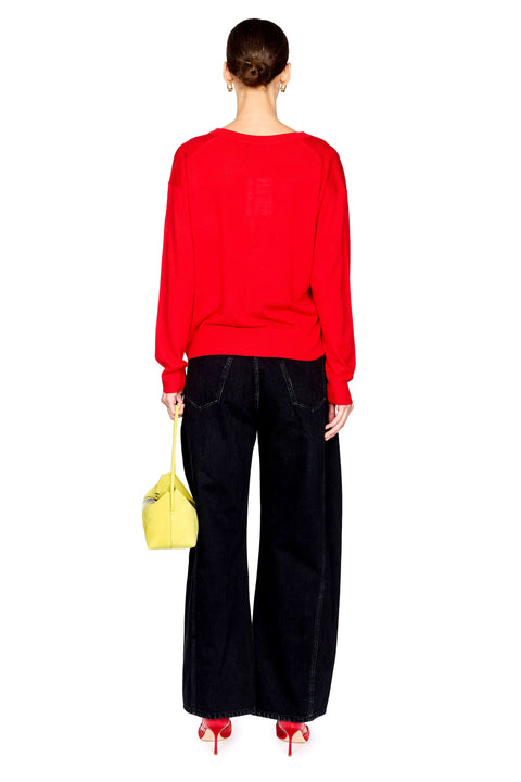 A model shown from the back wearing a bright red long-sleeve top, black wide-leg jeans, red high heels, and holding a small yellow handbag against a plain white background.