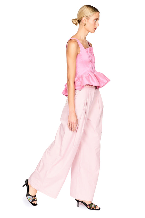 A woman modeling a light pink sleeveless top with a gathered peplum waist and matching wide-leg trousers, paired with black heeled sandals, against a plain white background.