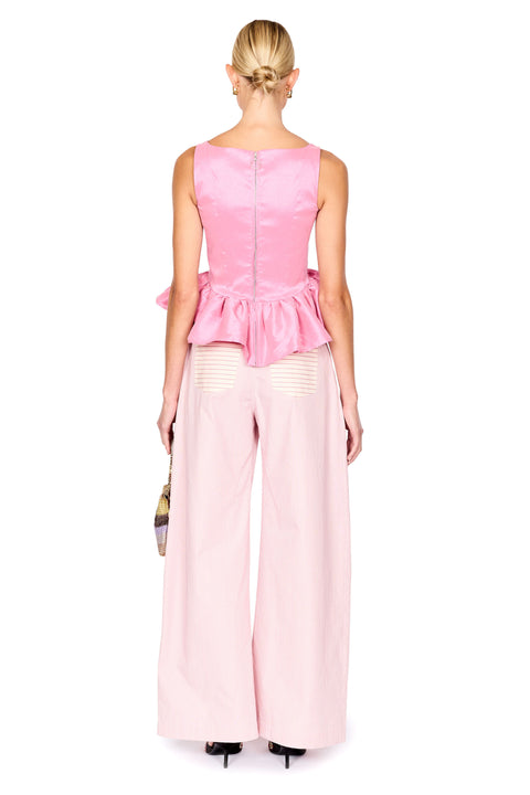 A woman shown from the back wearing a pink sleeveless top with a peplum waist and matching wide-leg trousers, standing against a plain white studio background.