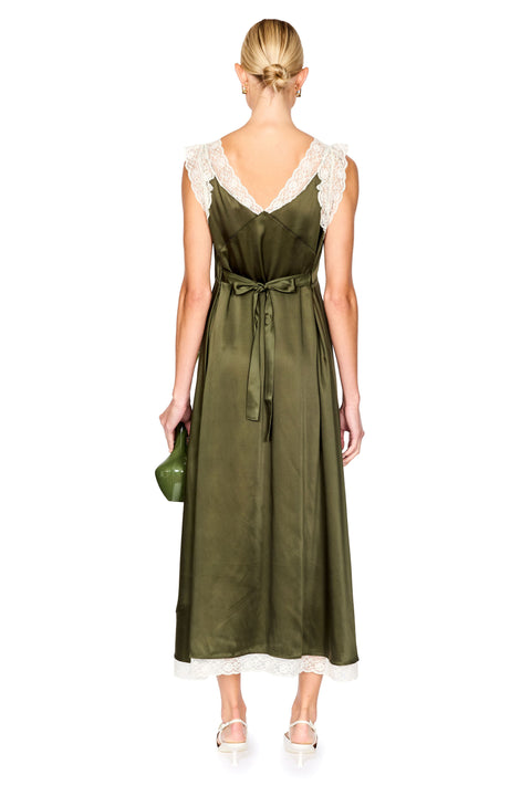 A woman shown from the back wearing an olive green satin midi dress with white lace shoulder details and a matching waist tie, holding a small green clutch against a plain white background.