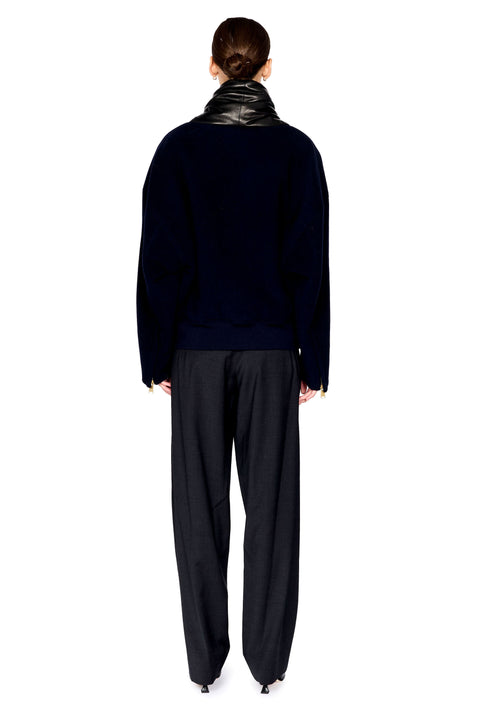 A model shown from the back wearing a dark navy knit jacket with a shiny black collar, paired with loose black trousers, against a solid white background.