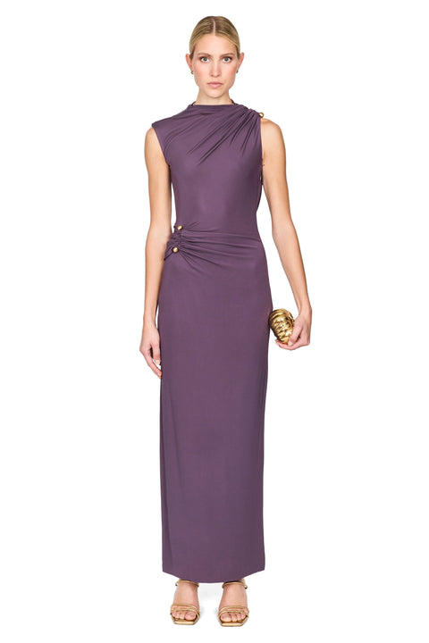 A woman modeling a sleeveless, high-neck, floor-length mauve dress with draped detailing and gold buttons, standing against a plain white background.