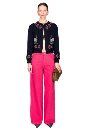 Woman wearing a black embroidered cardigan and pink pants on a white background centered stance