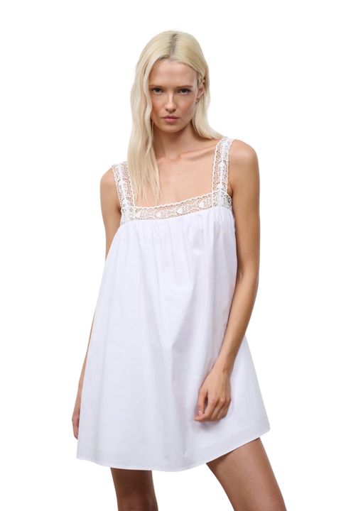 Woman wearing a white flowy mini dress with a lace trim on a white background