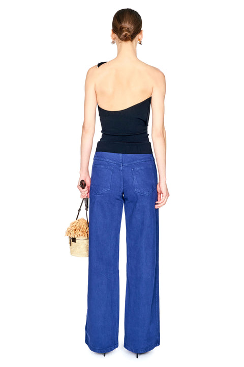 A woman shown from the back wearing a backless wired one shoulder black top with cobalt blue jeans and a black high heel