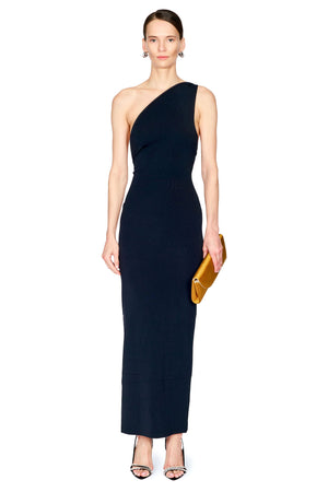 A model wearing a black one-shoulder bodycon maxi dress, holding a gold clutch and wearing black high-heeled sandals, set against a plain white background.
