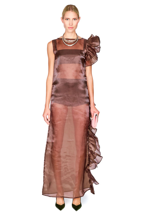 A model wearing a sheer, metallic bronze-brown midi dress with a ruffled shoulder detail and a matching ruffled side hem, paired with dark green pointed shoes and a layered silver necklace, set against a plain white background.
