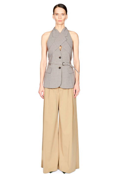A model stands against a white background wearing a sleeveless gray checked blazer vest with a belted waist and a beige wide-leg pants set.