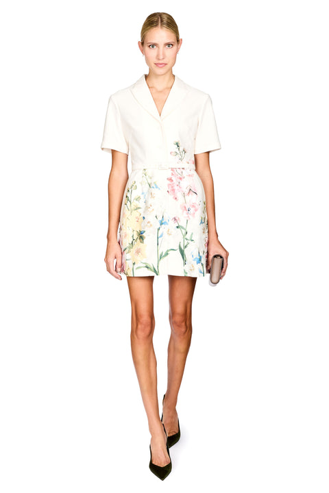 A woman modeling a white short-sleeve mini dress featuring a colorful pastel floral print, holding a small gray clutch against a plain white background.