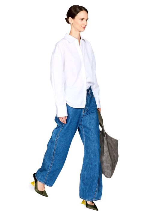 A woman modeling a white long-sleeve button-up shirt, wide-leg blue jeans, olive green pointed flats, and carrying a gray tote bag against a plain white background.