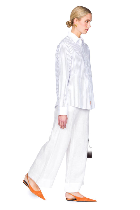 Woman wearing a striped shirt and white pants on a white background from the side.
