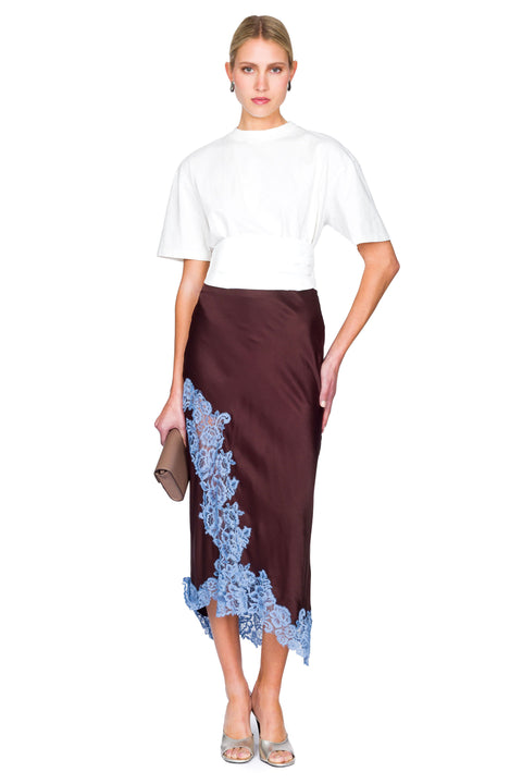 Woman wearing a white tuxedo top and brown skirt with blue lace details on a white background
