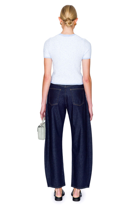 Woman wearing a light blue top with buttons and dark blue jeans on a white background from the back