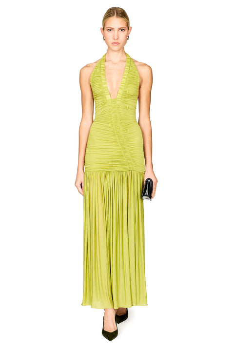 A model wearing a sleeveless halter-neck maxi dress in a vibrant lime green, featuring a ruched bodice and a pleated skirt, paired with black pointed-toe heels and holding a small black clutch against a solid white background.