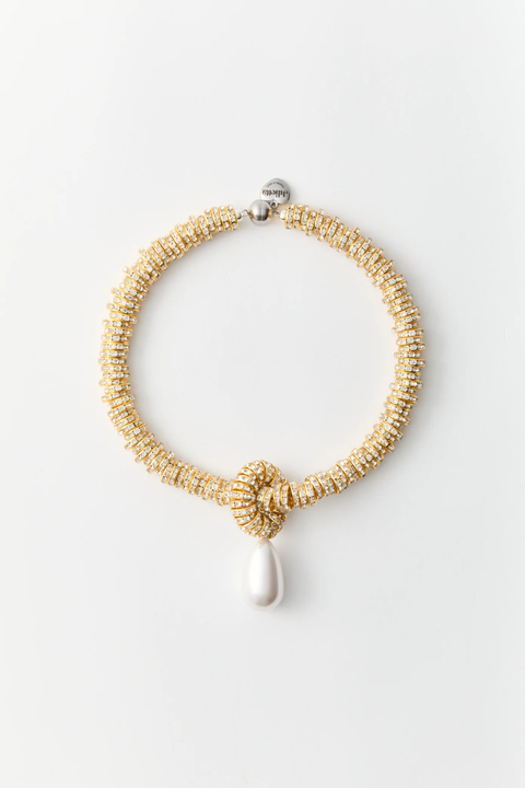 Gold beaded necklace with a white pendant on a light gray background