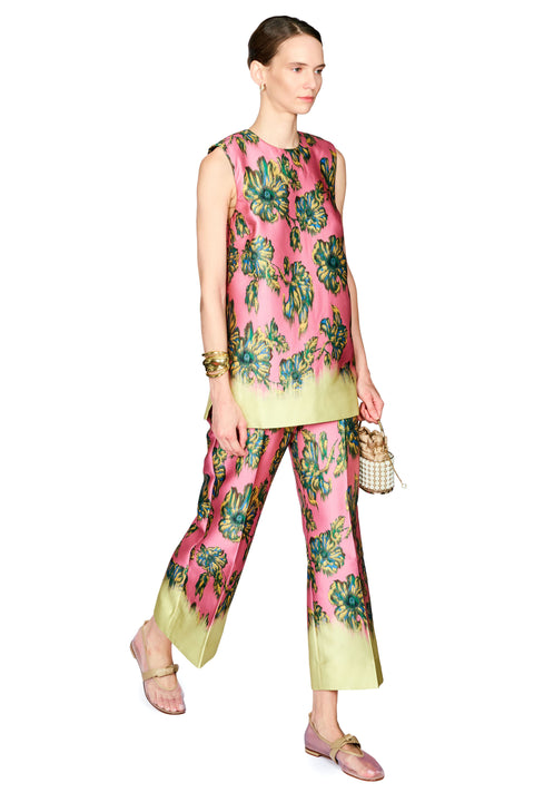 A model wearing a sleeveless pink matching set with a green and blue floral print and contrasting light green hems, styled with flat shoes and holding a small woven bag against a white background.
