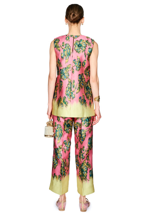 A model shown from the back wearing a sleeveless pink two-piece set with a green and blue floral print and a light yellow-green gradient hem. She is holding a small woven handbag against a solid white background.