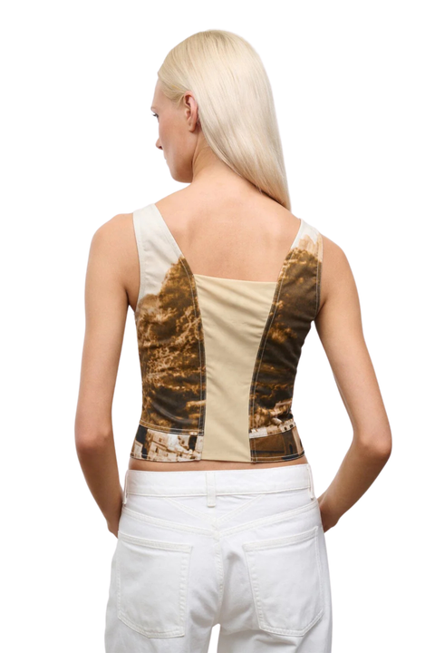 Woman wearing a patterned beige beach scene corset top and white pants on a white background